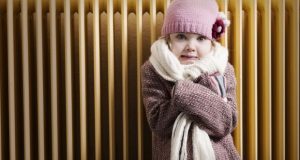 Rugged up child in front of heater